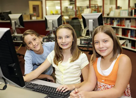 Three smiling students sitting at a computer